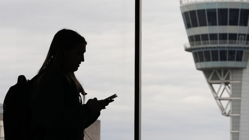 FILE - A traveler with a smartphone walks past an air traffic control tower at Philadelphia...